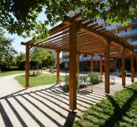 Dřevěná pergola s lavičkami v parku v Košicích, městská část Jih, obklopená zelení.