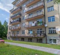 Pětipatrový bytový dům ve Vysokých Tatrách s balkony a zeleným trávníkem.