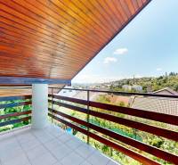 Balkon s dřevěným stropem s výhledem na střechy a zeleň v rodinném domě.