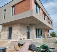 Rozestavěná vila ve Vodicích s betonovou a cihlovou fasádou, bazénem a verandou.