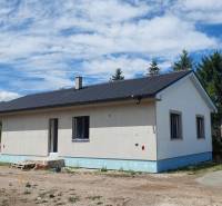 Rodinný dům v Kozárovciach s tmavou střechou obklopený zelení a stavebním materiálem.