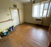 Interiér rodinného domu s dřevěnou podlahou, starším nábytkem a zavěšeným svítidlem.