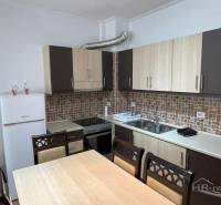 Kuchyně v rekreačním apartmánu s jídelním stolem a bílými spotřebiči.