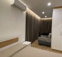 Interiér rekreačního apartmánu s postelí, pohovkou, závěsy a klimatizací.