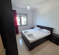 Ložnice v rekreačním apartmánu s manželskou postelí, nočními stolky a oknem s červenými závěsy.