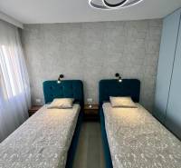 Dvoulůžková ložnice s geometrickou tapetou a moderním osvětlením v rekreačním apartmánu.