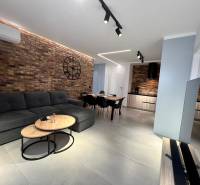 Obývací pokoj v rekreačním apartmánu s cihlovou stěnou, pohovkou a televizí.