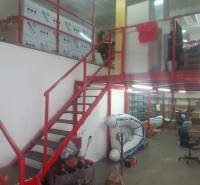 Interiér skladu s regály, lodí a červeným schodištěm.