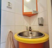Oranžové umyvadlo s kulatým žlutým okrajem, zrcadlo a věšák s ručníkem.