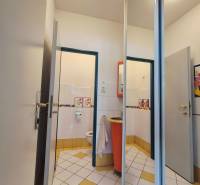 Toaleta s bílými a žlutými dlaždicemi a oranžovým umyvadlem v obchodních prostorách.