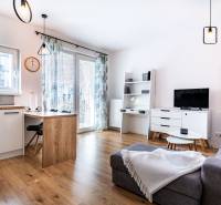 Obývací pokoj v 2pokojovém bytě s pohovkou, TV, jídelním stolem a moderními lampami.