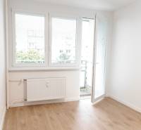 Ve 2-pokojovém bytě je světlá místnost s balkónovými dveřmi a dřevěnou podlahou.