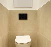 Závěsné WC v 2-pokojovém bytě, béžové obklady, černé splachovací tlačítko.