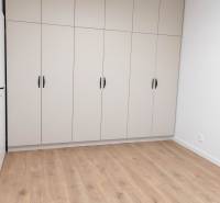 Bílá vestavěná skříň se šesti dveřmi v 2-pokojovém bytě na dřevěné podlaze.