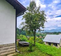 Výhled z chaty v Mojši ukazuje střechy, zeleň a vzdálené kopce pod oblačnou oblohou.