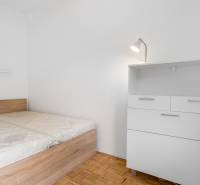 Ložnice s postelí a komodou v 2-pokojovém bytě, podlaha s dřevěným dekorem.
