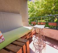 Balkon s dřevěnými paletami a kovovým stolem ve 4pokojovém bytě.