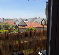 Balkon v 3-pokojovém bytě s ratanovým nábytkem a výhledem na střechy.