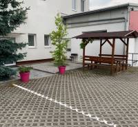 Dvorec s dlažbou, dřevěné sezení a rostliny v růžových květináčích na ulici Šamorínska.