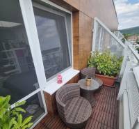 Balkon 1-pokojového bytu s ratanovým nábytkem a rostlinami u posuvného okna.
