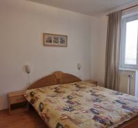 Ložnice ve 4pokojovém bytě s manželskou postelí, obrazem a balkónovými dveřmi.