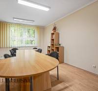 Jídelní stůl s knihovničkou a kancelářskými židlemi v kanceláři.