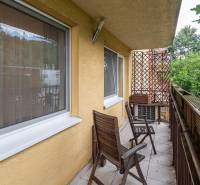 Balkon 4pokojového bytu s dřevěným nábytkem a zeleným výhledem.