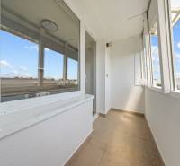 Světlý balkon 2-pokojového bytu s výhledem na okolní střechy a modrou oblohu.