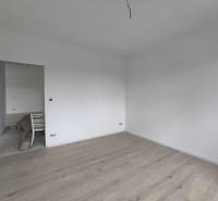 Prázdný pokoj s bílými stěnami a světlou dřevěnou podlahou v rodinném domě.