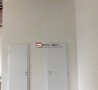 Dvojité bílé dveře v obchodních prostorách s betonovým stropem.