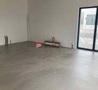 Nezařízené obchodní prostory s velkými okny a betonovou podlahou.