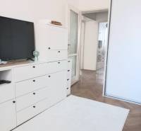 Bílý obývací pokoj ve 4pokojovém bytě s TV, skříňkami a dřevěnou podlahou.