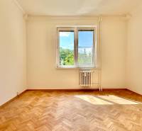 Prázdný pokoj v třípokojovém bytě s parketami a oknem s výhledem na zeleň.