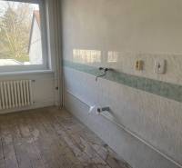 Prázdná kuchyně v rodinném domě s dlaždicemi a dřevěnou podlahou.