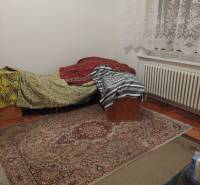 Pokoj v rodinném domě s postelí, kobercem a krajkovými záclonami.