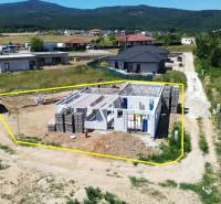 Stavba rodinného domu v Trenčianském Jastrabí, obklopená venkovskou krajinou a sousedními domy.