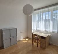 Osvětlený pokoj v 2-pokojovém bytě se stolem, židlí a skříňkou na parketové podlaze.