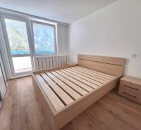 Světlá ložnice s dřevěnou postelí a nočními stolky v 2pokojovém bytě.