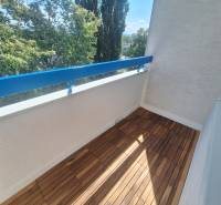 Balkon s dřevěnou podlahou a výhledem na stromy v 2-pokojovém bytě.