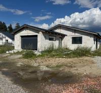 Nedokončený rodinný dům ve Valči s garáží obklopený přírodou a stavebním materiálem.