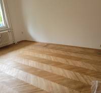 Prázdný pokoj v třípokojovém bytě s parketovou podlahou a oknem.