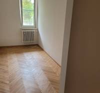 Pokoj v 3-pokojovém bytě s dřevěnou podlahou a radiátorem pod oknem.