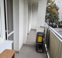 Balkon v 3-pokojovém bytě se skládacími židlemi a výhledem na stromy na dvoře.