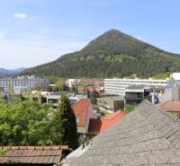 Na ulici Nám. A. Hlinku je vidět střechy, budovy a zalesněný kopec za Rodinným domem.