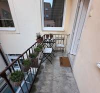 Úzký balkon s kovovým zábradlím, židlemi a květináči v 2-pokojovém bytě.