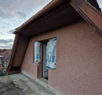 Stavební detail na fasádě rodinného domu, okno, exteriér, střecha a pozadí krajiny.