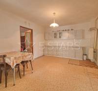 Kuchyně v rodinném domě s jídelním stolem, kuchyňskou linkou a vzorovanou podlahou.