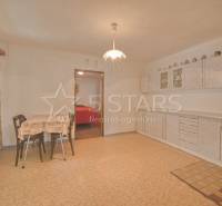 Kuchyně v rodinném domě s jídelním stolem, závěsy a kuchyňskou linkou.