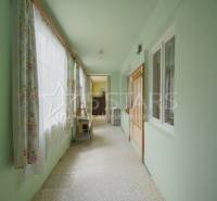 Interiér rodinného domu s úzkou chodbou, záclonami a světle zelenými stěnami.
