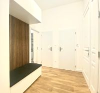 Interiér 3-pokojového bytu s podlahou s dřevěným dekorem, dřevěným obkladem a bílou vestavěnou skříní.